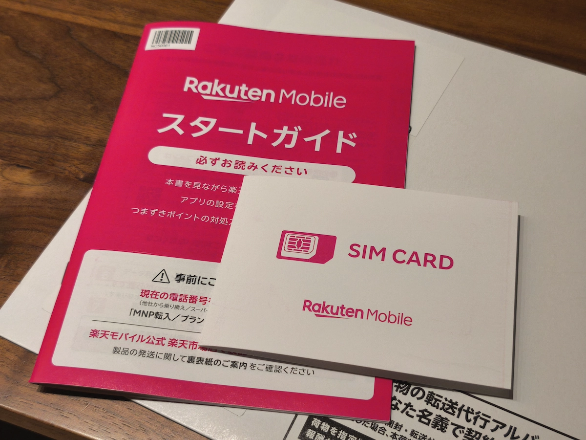 「テーブルの上に置かれた楽天モバイルのスタートガイドとSIMカード封筒。ピンクの冊子に『必ずお読みください』と書かれ、白い封筒には『SIM CARD』の文字とRakuten Mobileロゴが印刷されている。