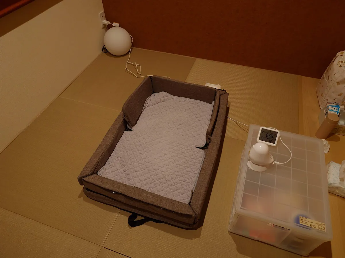 旅行先の和室に設置された、赤ちゃん用のポータブルベッドとベビーモニター。安心して眠れるように準備された快適な空間。
