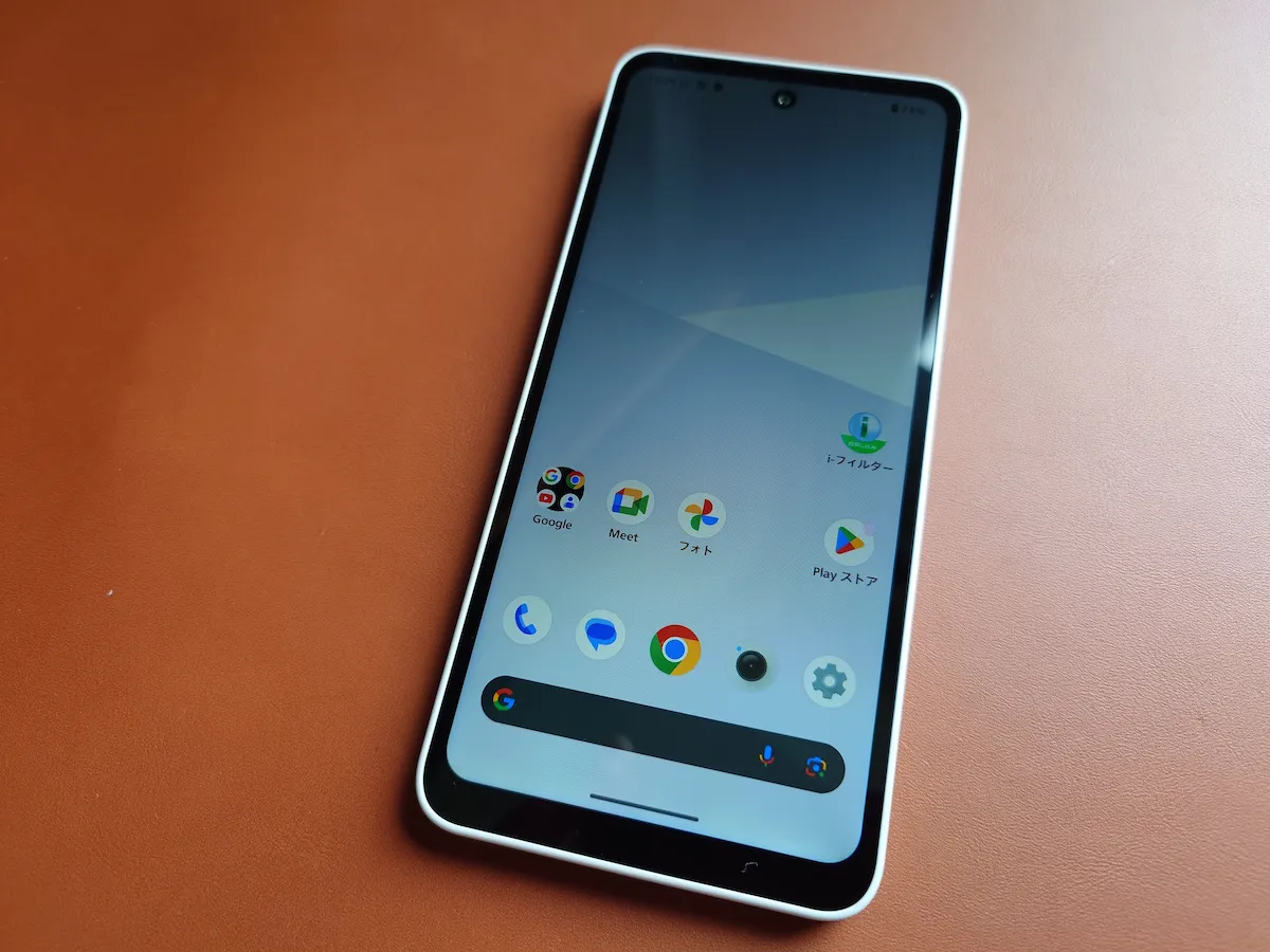 AQUOS wish5のホーム画面を表示した前面、木目デスク上での使用シーン、薄型で持ちやすい印象の写真