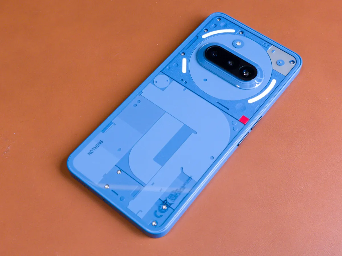 Nothing Phone (3a) ブルーの背面Glyph LEDを点灯しブラウンデスクに置いた写真