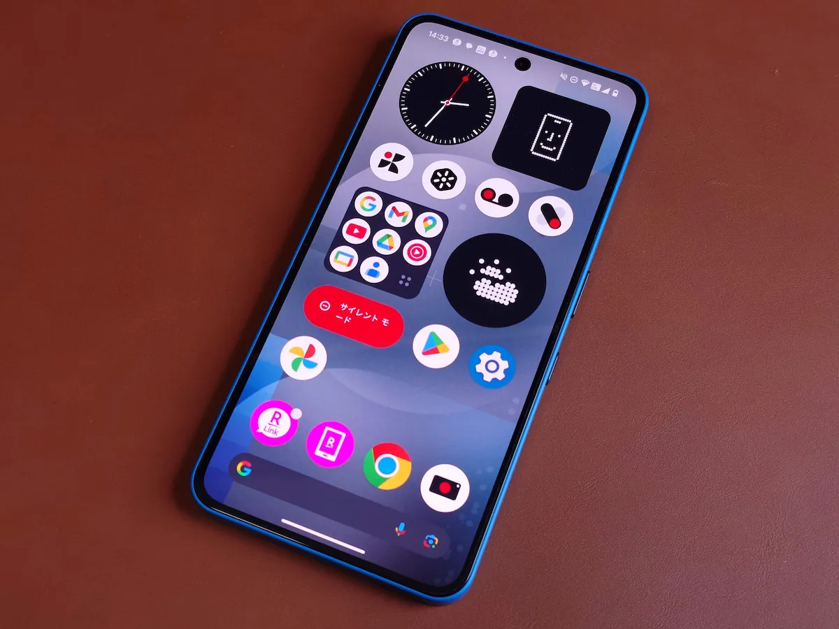 Nothing Phone (3a) ブルーのホーム画面を点灯しブラウンデスクに斜め配置した様子を撮影した写真
