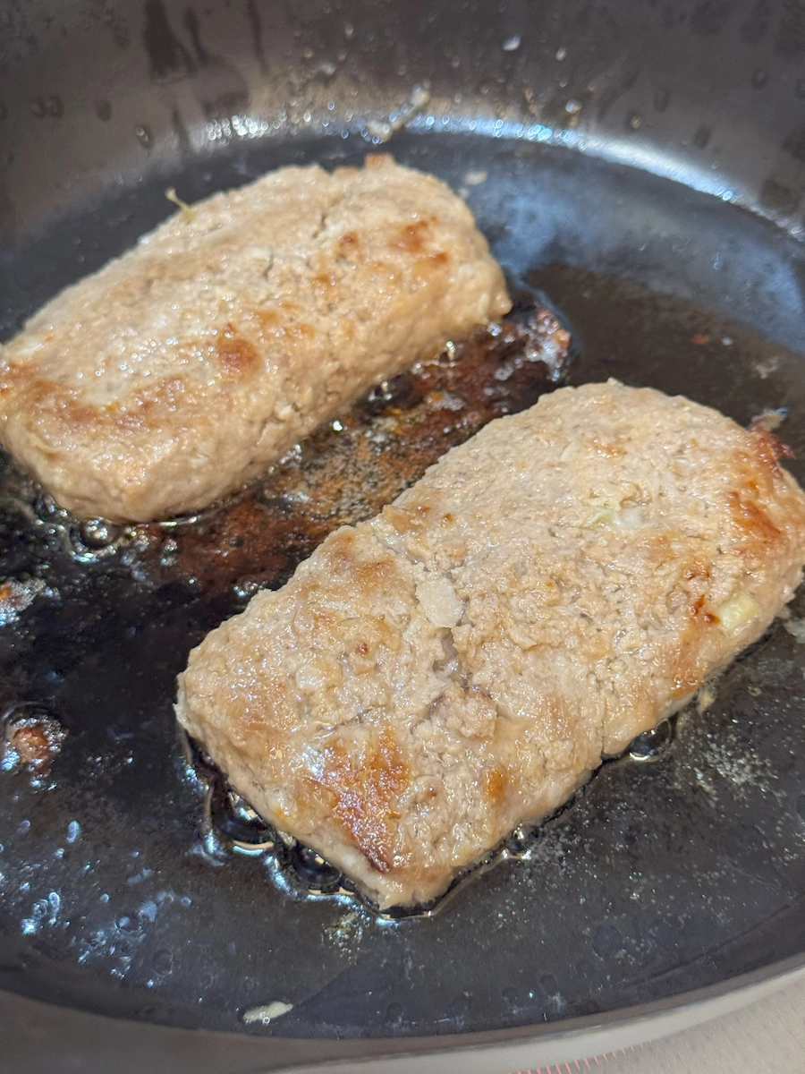 熱したフライパンで長方形ハンバーグ2個を焼成、香ばしい焦げ目とにじむ肉汁が見える接写