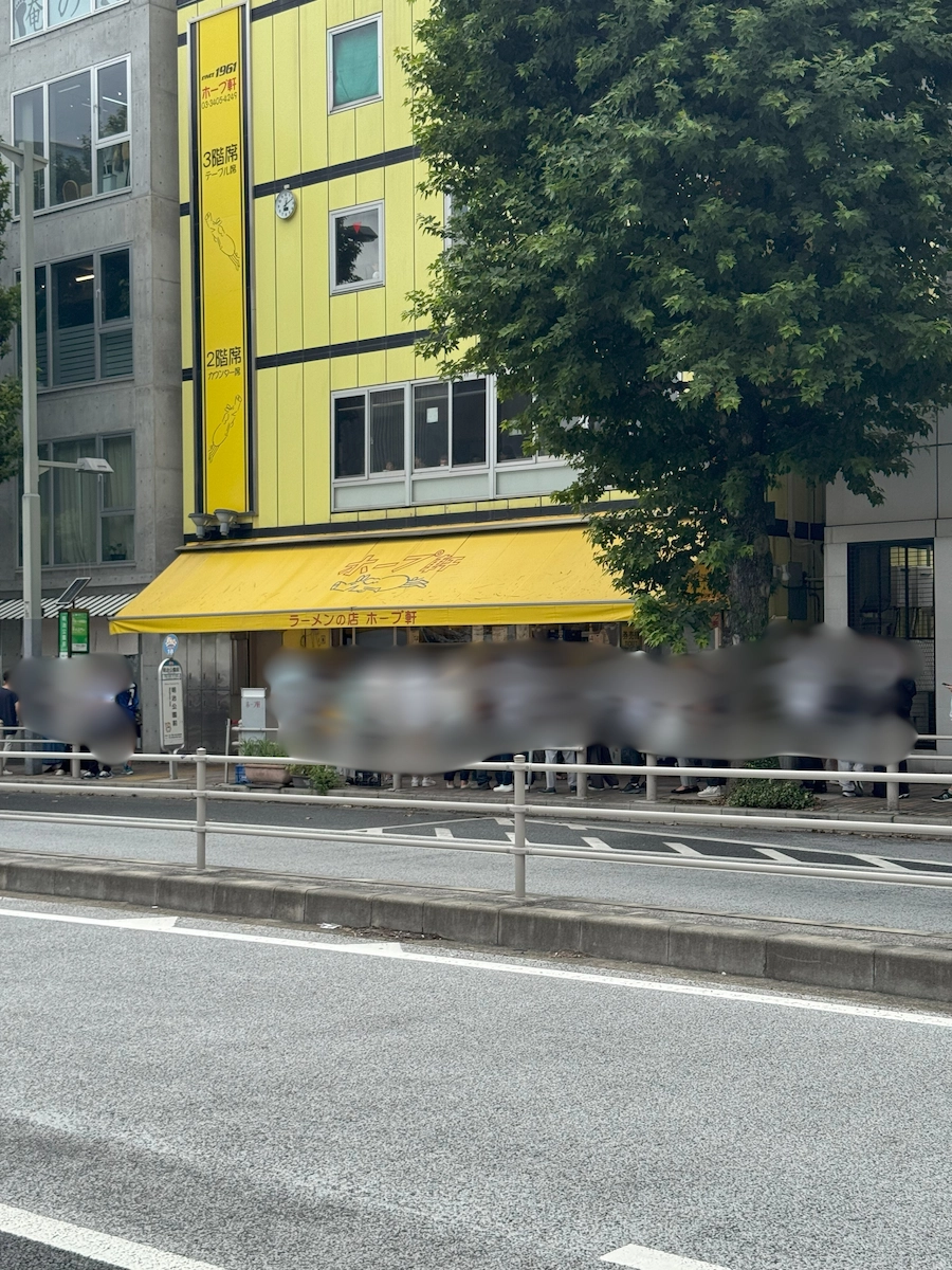 東京・ラーメンの丘ホープ軒の黄色い建物外観。道路沿いに行列ができている様子を撮影